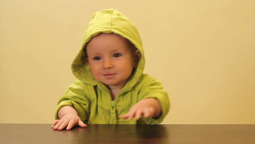 Little cute child with green hood practicing the stand up at the edge of the table