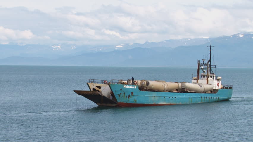 HOMER, AK - CIRCA 2012: A weatherworn landing craft on approach to the harbor with its cargo of a diesel tractor truck and four tank trailers.