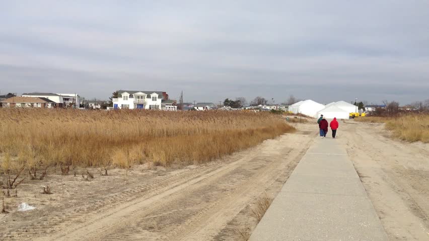 Hurricane Sandy Establishing shot of Breezy Point town from the beach in Queens. A concrete walkway is covered with sand from waves and storm surge by Hurricane Sandy. People walk along beach to town.