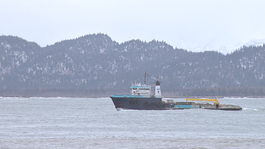 HOMER, AK - CIRCA 2012: An impressive and imposing heavy-duty tug/utility vessel returns to the calmer bay, passing a rolling container barge being towed by a smaller tug.