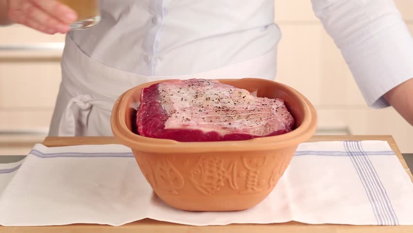 Stock and white wine being added to beef in a terracotta baking dish
