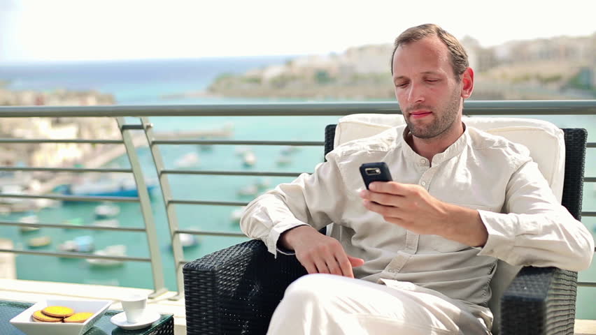 Young man drinking coffee and using smartphone on terrace
