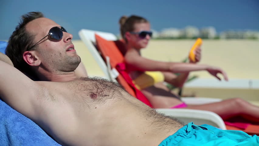 Man sunbathing on sunbed, woman applying sun block lotion
