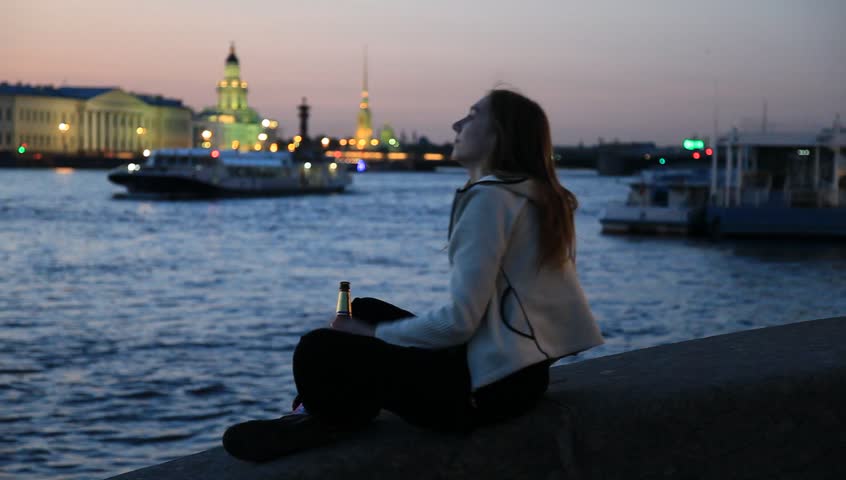 Smiling girl with bottle beer on embankment at white night in St. Petersburg, Russia. The focus changing to architectural background at the end. 1080p