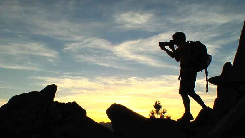 Silhouette of a man with a backpack taking pictures of nature on rocky terrain in the mountains of the American wilderness