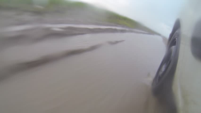 Driving in the rain on a road with puddles and muddy water