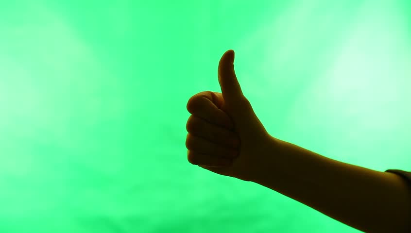 Young adult woman signals Ok!  against green screen chroma background. Back-lit silhouette.
