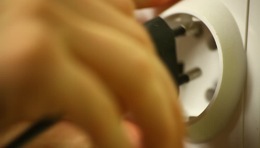 Young adult woman hand pulls plug out of wall plug.
