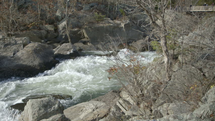 Scene follows the churning waters of a river to an expanse of wilderness lining the rocky riverbanks.