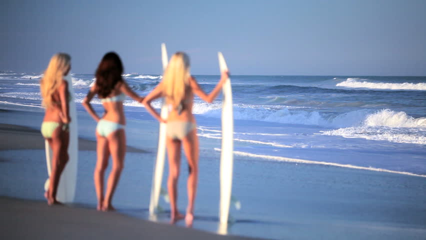 Three beautiful slim girlfriends with surfboards waiting for the waves