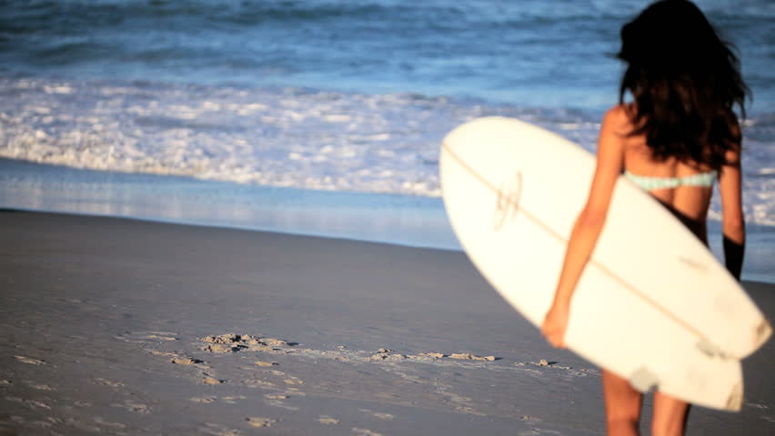 Two beautiful slim girlfriends walking to the ocean with surfboards