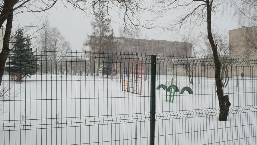 playground and other kindergarten preschool toys in winter over fence. snowstorm blizzard snow fall. holiday time.