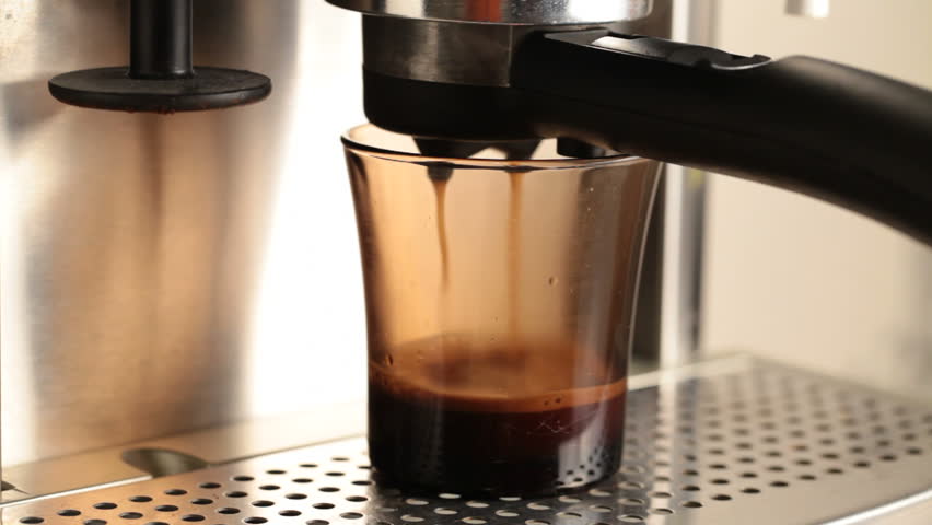 Coffee pours in dark glass cup in espresso coffee machine