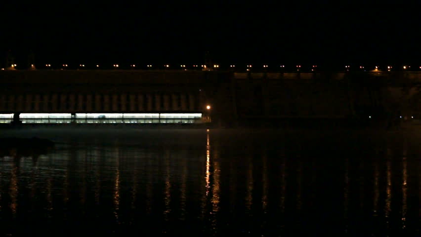 Dam of Krasnoyarsk Hydropower Plant at night, medium shot. Halogen illumination reflecting in water of Yenisei river, against black night sky. Town of Divnogorsk, Russia. January 14, 2013.
