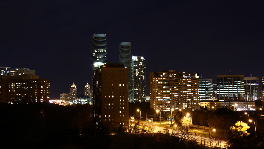 Moonset Over City Timelapse 1. Night moon setting over a small downtown cityscape. Shot in time-lapse with traffic and lights going off as the gets late.