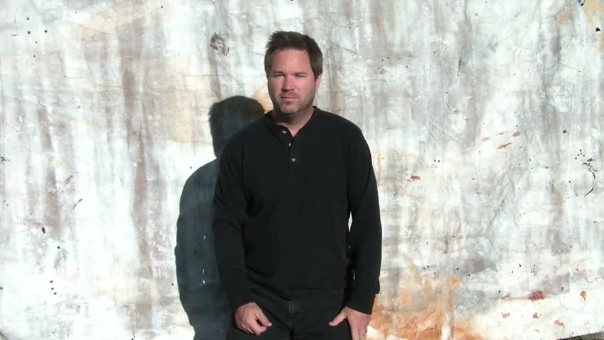 Man puts thumb up in approval, smiling with sun lighting his black clothing and canvas as a backdrop.