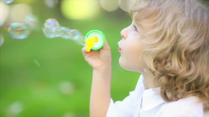 Happy child blowing soap bubbles in spring park. Slow motion