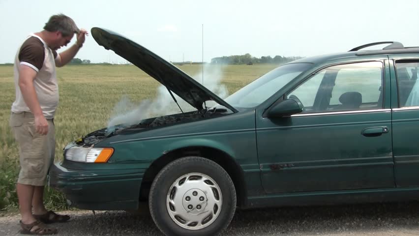 With car broken down, man approaches hood in country, opens it with smoke emitting from underneath, turns towards camera with frustration, in daylight.