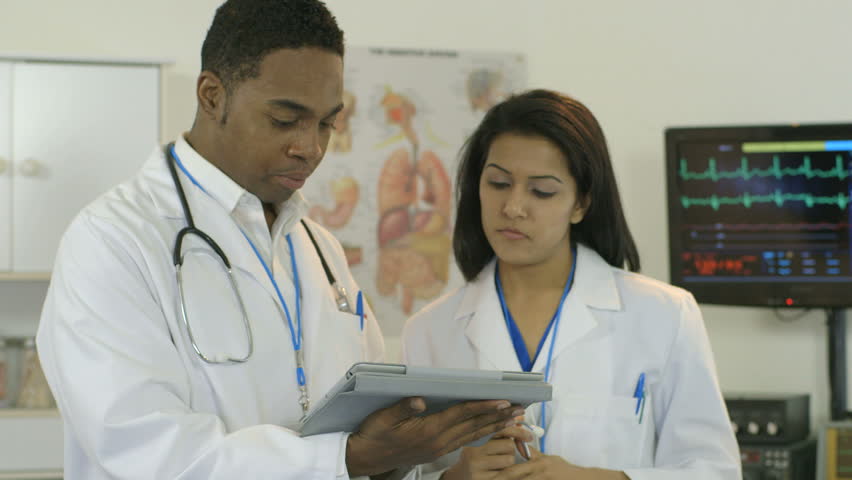 A lovely physician of South Asian ethnicity finishes consulting with a colleague and listens to the breathing of an older female patient lying in a hospital bed.