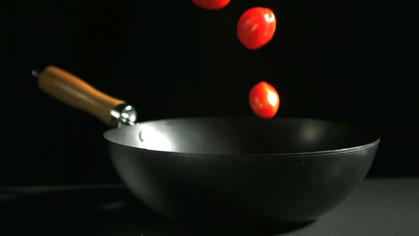 Cherry tomatoes falling into wok in slow motion