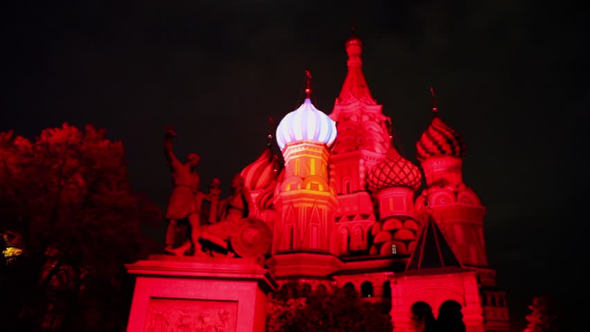 Illumination on colorful cupolas of St. Basils Cathedral with monument of Minin and Pozharsky in red light at night in Moscow