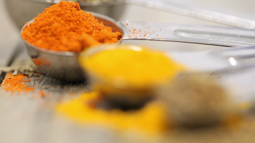 Various mixed spices (oregano, curcuma, paprika, anise) in metal scoops on wooden table