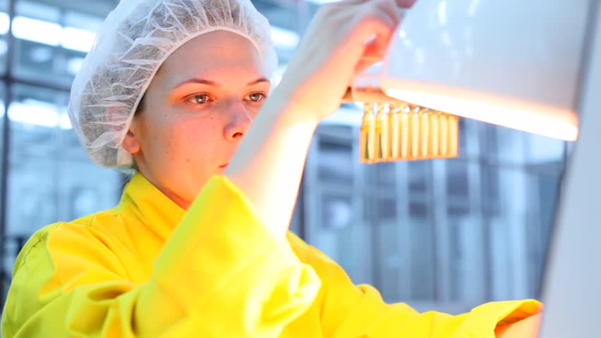 Technician inspecting the quality of glass ampoules at a pharmaceutical plant.