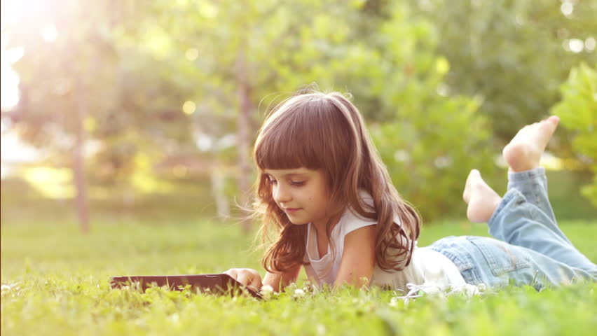 Girl with a touchscreen lying on the grass in sunny lights. Lens flare.