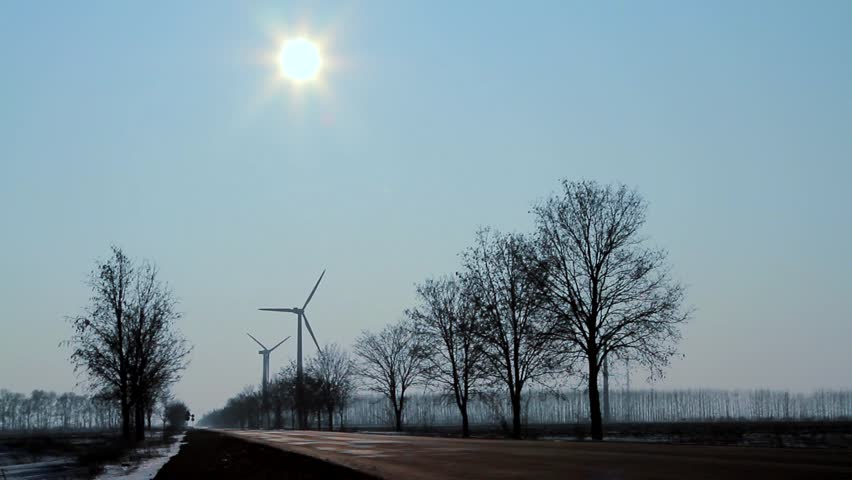 Concept: advantages of the green energy. Hybrid car overtaking fossil fuel car toward wind turbines and bright sun. Northeast Bulgaria.