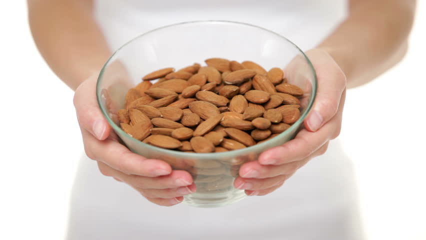Almonds nuts - woman showing raw almond bowl closeup. Healthy food concept in studio with hands lifting bowl of unprocessed almonds up to focus on white background.