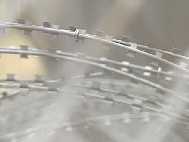 Roll focus from barbed wire to chain link fencing.