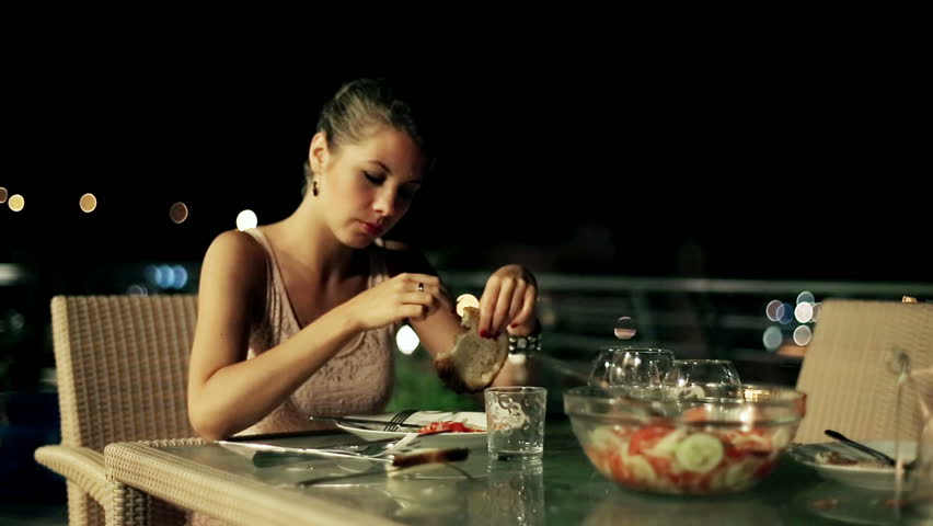 Sad woman eating dinner on the terrace at night, steadycam shot

