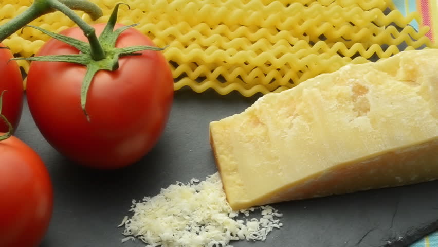 Close-up camera dolly across Italian recipe ingredients: fresh tomatoes, pasta, Parmesan cheese and rosemary.