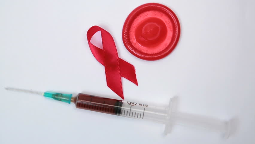 Red ribbon condom and syringe with blood sample on revolving white surface