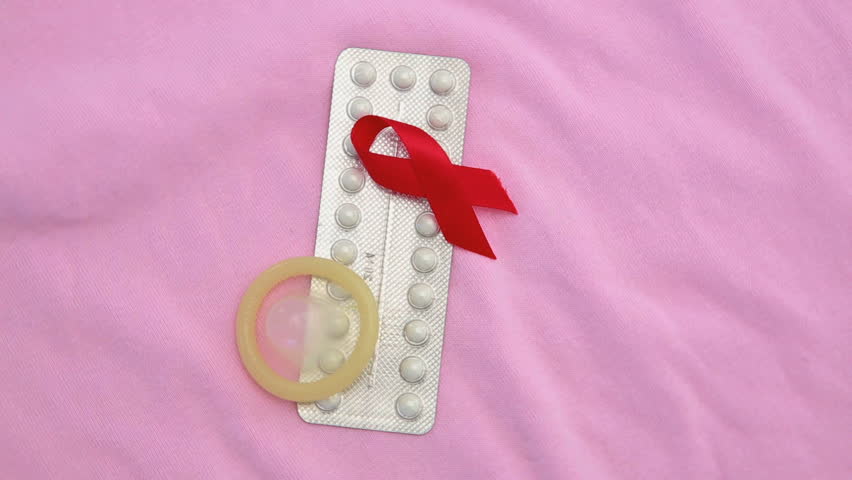 Contraceptive pill packet with condom with red ribbon on revolving pink blanket