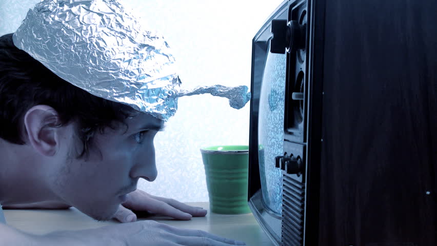 Crazy young man with a tinfoil hat watching a TV tuned with fuzzy reception, probably seeing aliens.