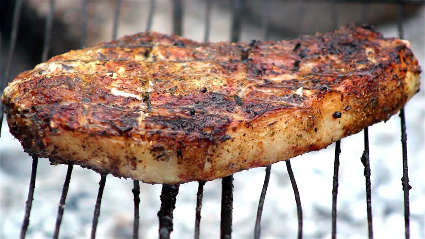 Juicy steak sizzle on flaming and smoking grill,pork steak on a grill