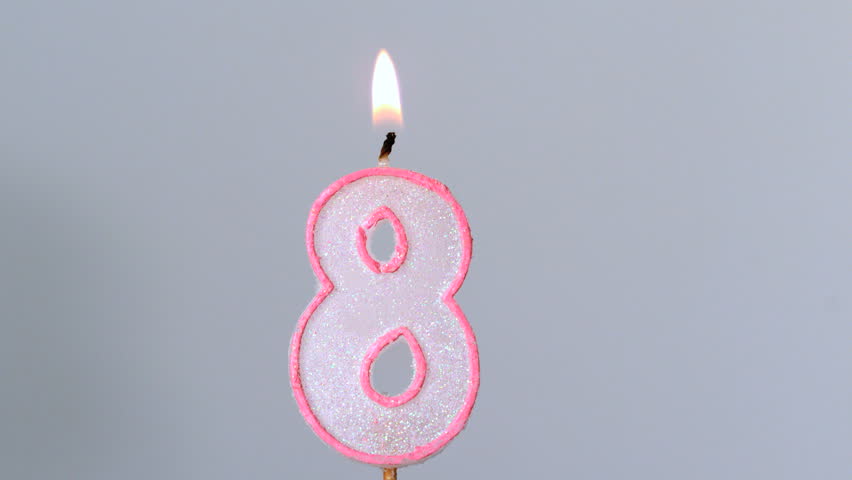 Eight birthday candle flickering and extinguishing on grey background in slow motion