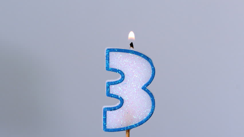Three birthday candle flickering and extinguishing on blue background in slow motion