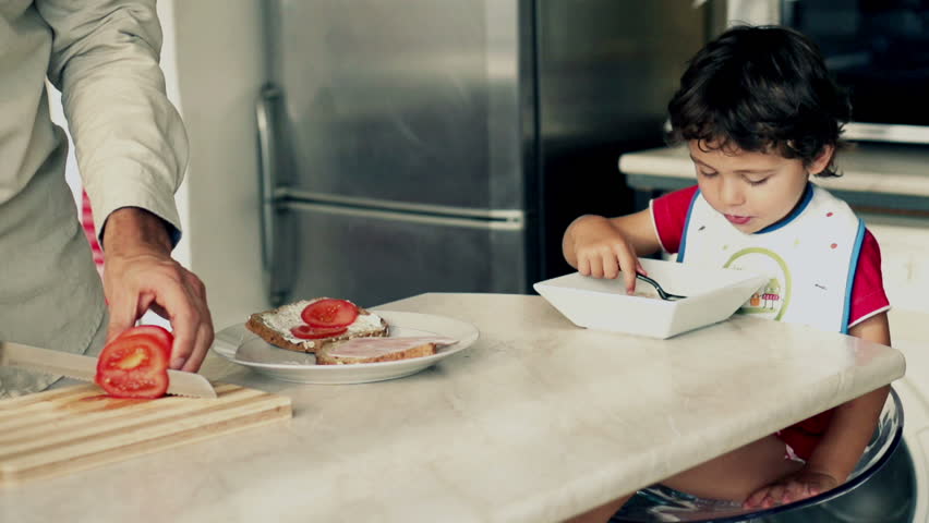 Little boy eating cornflakes with milk, father preparing sandwich, slow motion shot at 240fps
