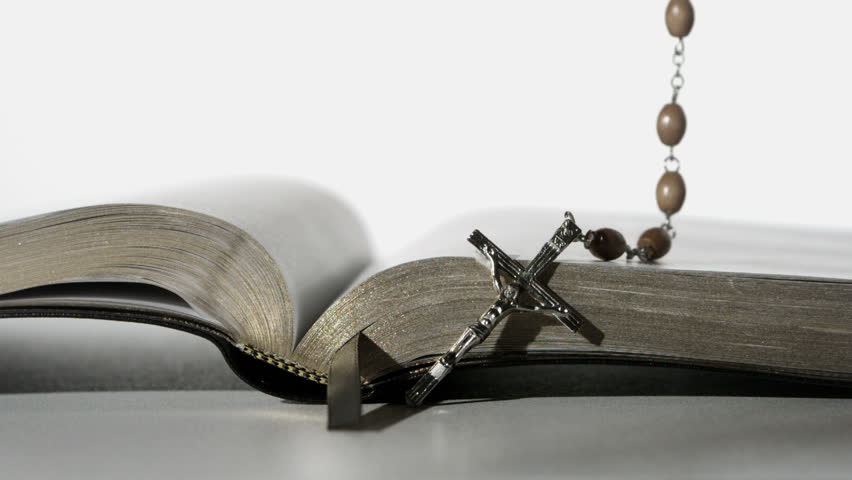 Rosary beads falling onto open bible on white background close up in slow motion