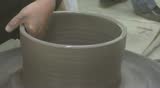 Two hands are molding clay into a vase.