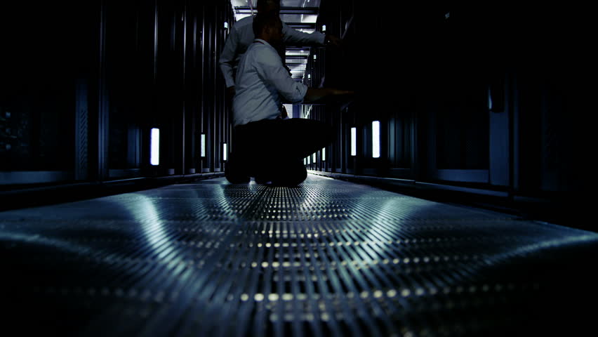 Time lapse of a team of people working in a data center with rows of server racks and super computers. They are looking into data cabinets and checking cables and other equipment. 