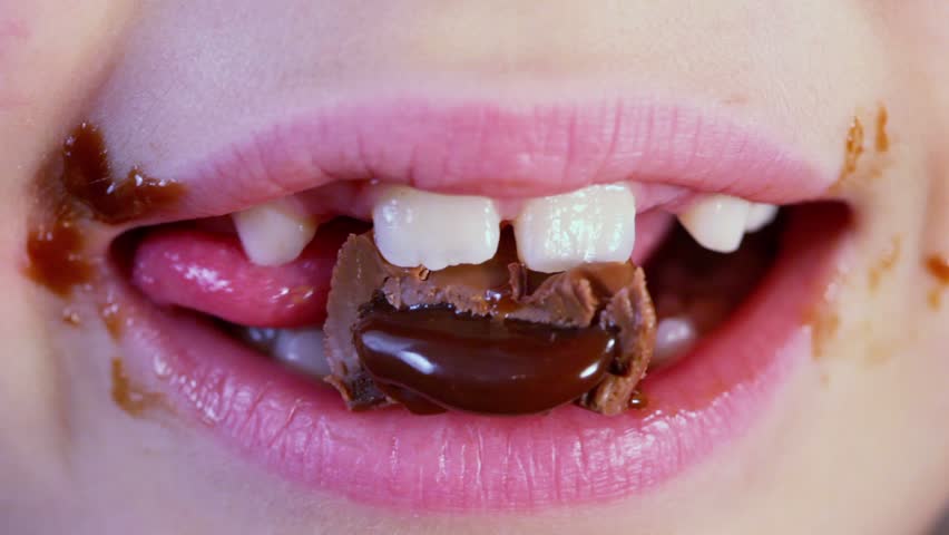 Smeared childish mouth chews chocolate candy, closeup
