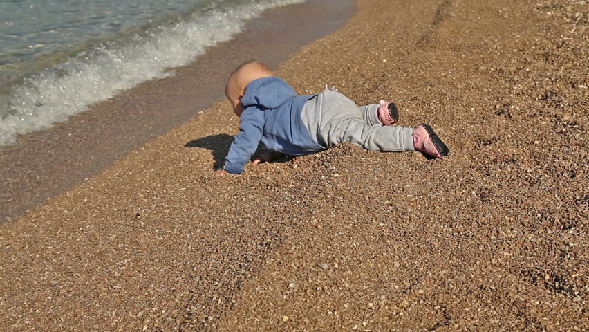 Baby crawl on the beach bravely going toward wavy sea.
