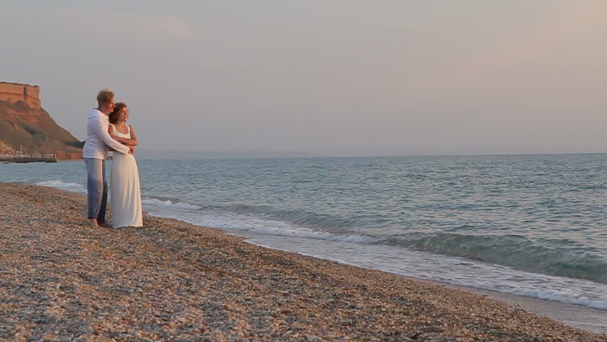 Two shots: first â happy couple is strolling on the beach, second â back view of young couple, enjoying beautiful sunset