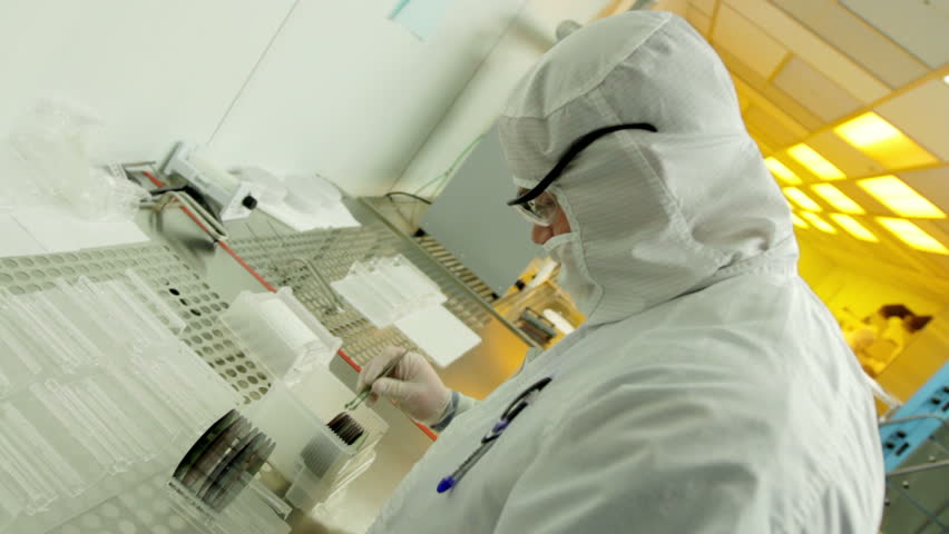 Scientist / technician preps silicon wafers to go into a kiln during silicon chip manufacture in a clean room. They are wearing full body white "bunny suit" coveralls to avoid contamination. 