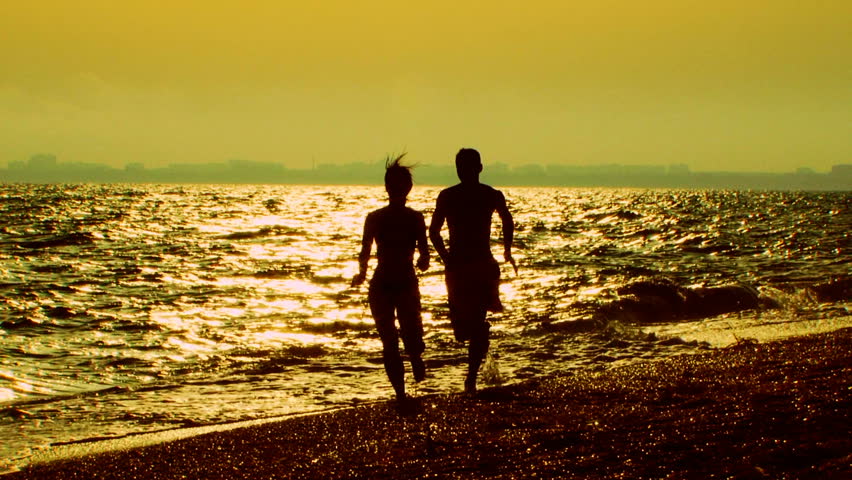 In the shadows. The young pair runs on the beach. The guy catches up with the girl and playfully throws her to the ground. they then run back. 
