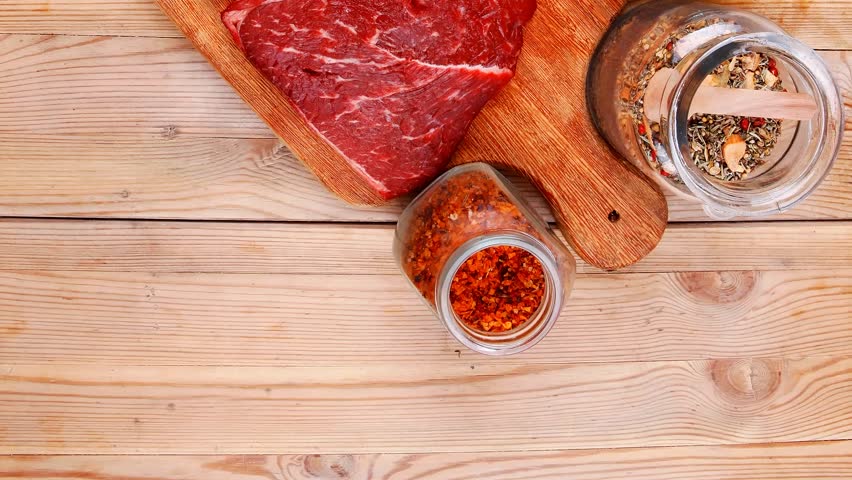 fresh raw beef meat fillet flesh with peppercorn and thyme ready to grill on wood figured old style board over table with spices in glass
