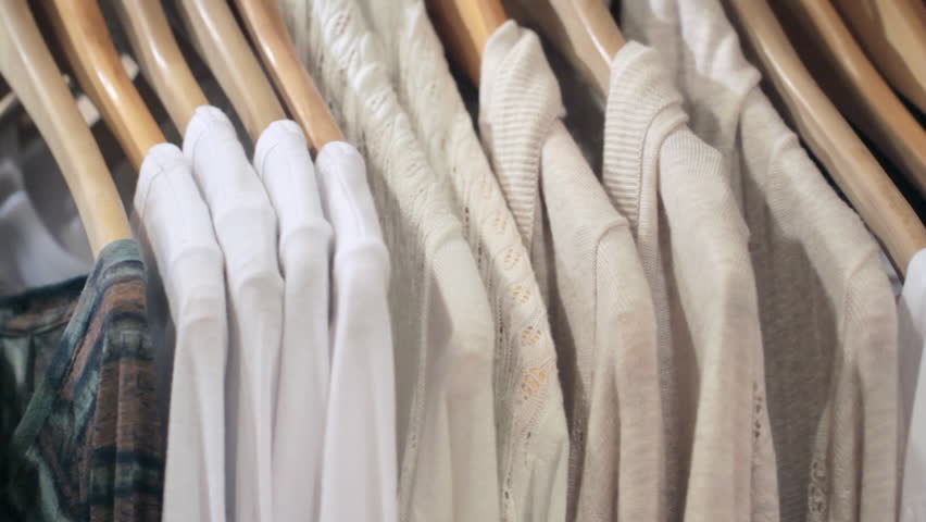 Woman's hands run across a rack of clothes, browsing in a boutique. Dolly shot from the side.